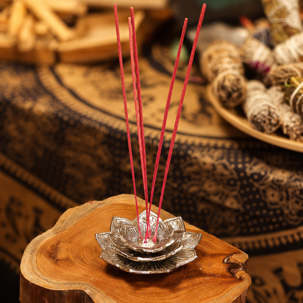 Lotus flower incense stick holder with incense sticks on a log surface, smudge sticks and patterned fabric in the background – spiritual décor from CardsAmoreStore.